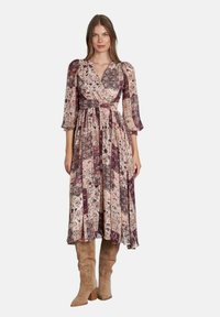 Abito maxi con stampa floreale in tonalità di rosa e viola; design a scollo a V, maniche puff 3/4, vita marcata, gonna fluida, abbinato a stivali beige.