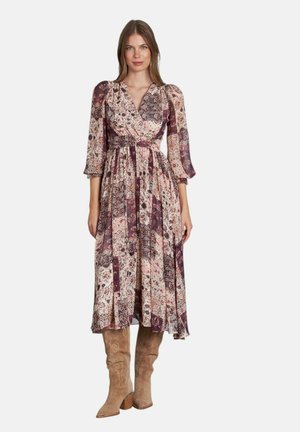 Maxi vestido con estampado floral en tonos de rosa y púrpura; diseño de escote en V, mangas abullonadas de 3/4, cintura ceñida, falda fluida, combinado con botas beiges.