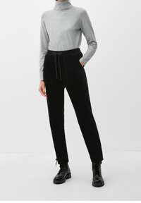 Pantalon en velours côtelé noir avec taille à cordon de serrage et deux poches avant, associé à un pull en cachemire gris clair. Des bottes complètent la tenue.