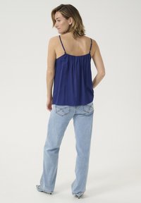 Mornarsko modra lahka kamizola z tankimi nastavljivimi naramnicami, nabranim korpusom, v kombinaciji z poškropljenimi širokimi kavbojkami z okrasnim šivanjem.