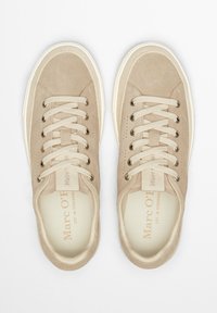 Beige suede sneakers with round toe, flat laces, metal eyelets, and a textured design. Includes a branded tongue and white rubber sole.