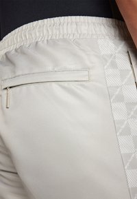 Pantalones cortos de color gris claro con tejido texturizado, cinturilla elástica, bolsillo trasero con cremallera y un panel lateral que presenta un patrón geométrico.