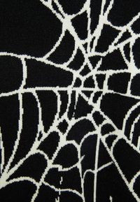 Svart tyg med ett vitt spindelnätsmönster med intrikata linjer och former, som visar en strukturerad stickad finish.