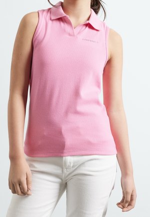 Polo rose côtelé sans manches porté avec un pantalon blanc sur une personne, montrant le haut du corps et les bras sur un fond uni.