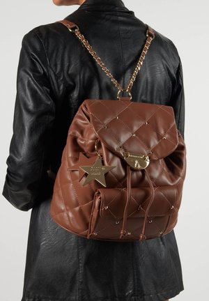 Brauner, gesteppter Leder-Rucksack mit Kordelzugverschluss, goldenen Beschlägen, einem sternförmigen Anhänger und Kettenriemen. Texturiertes, vielseitiges Design.