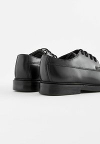 Chaussures en cuir noir avec une finition lisse, bout arrondi et détails de lacets. Elles présentent un petit talon empilé et des accents de couture subtils.
