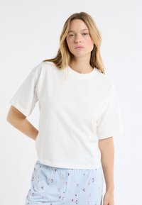 Biały bawełniany t-shirt z krótkimi rękawami i okrągłym dekoltem. Połączony z jasnoniebieskimi szortami z kolorowym, zabawnym wzorem.