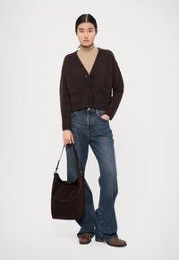 Brown knitted cardigan with a V-neck, button-down front, and pockets, paired with light blue flared denim and a dark brown shoulder bag.