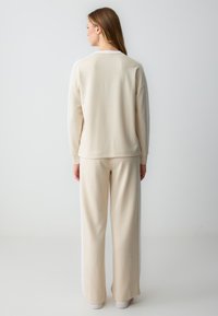Felpa beige a maniche lunghe con collo rotondo, abbinata a pantaloni larghi beige coordinati. Materiale morbido, design minimalista, senza motivi visibili.