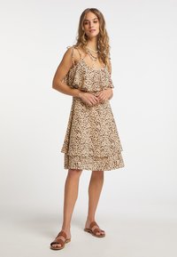 Dejardrakt med leopardtryck i beige, med lager av volanger, spaghettibandsremmar och en avslappnad passform. Bärs med bruna platta sandaler.