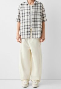 Lyhythihainen, ruutukuosisessa kreemivalkoisessa ja mustassa puuvillapaidassa, yhdistettynä kreemivärisiin leveälahkeisiin housuihin ja valkoisiin tennareihin. Rentoa, väljä istuvuutta.