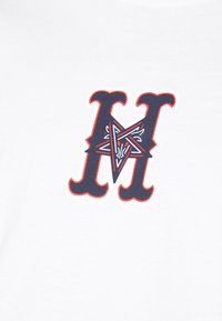 T-shirt blanc arborant une grande lettre "M" bleu marine avec des motifs complexes à l'intérieur et une bordure rouge, imprimé sur un tissu doux.