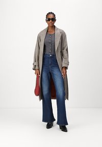 Γκρι μάλλινο παλτό, εφαρμοστό γκρι τοπ με κουμπιά, μπλε τζιν με ψηλή μέση και κλος, μαύρες ψηλές μπότες, κόκκινη τσάντα και γυαλιά ηλίου.