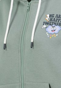 Groene rits-hoodie van zachte stof met witte trekkoorden. Bevat een grafisch ontwerp van een glimlachende wolk met de tekst "WE ARE HAPPY TOGETHER."