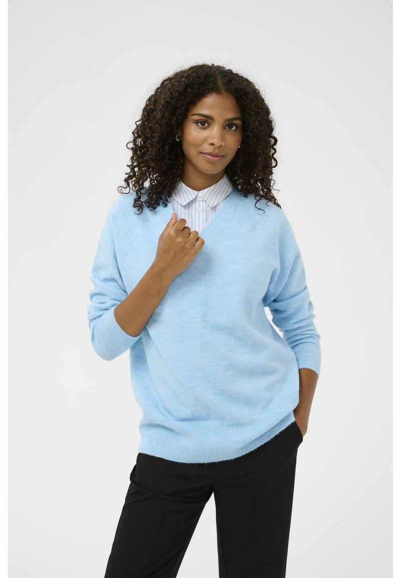 Gaiši zils v-veida džemperis mīkstā materiālā, ar ribotām aprocēm un apakšmalu. Apvienots ar melnajām biksēm, radot brīvu piegriezumu.