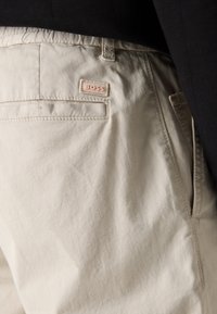 Shorts en coton beige avec une poche arrière ornée d'une étiquette rose. Le tissu présente une texture lisse et un design décontracté.