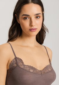Lace-trimmed brown camisole with ribbed texture, featuring thin adjustable straps and floral lace accents along the neckline.