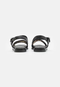 Sandales en cuir noir avec deux larges brides, boucle argentée réglable et semelle plate en caoutchouc. Design minimaliste, arrière ouvert pour un enfilage facile.