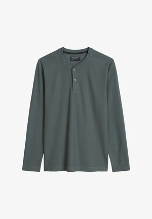 Donkergroene henley met lange mouwen, gemaakt van geribd stof. Heeft een ronde halslijn, twee knopen op de borst en zijsplitten aan de zoom.