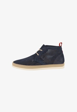 Scarpa traforata blu navy con suola beige, dotata di un tassello rosso sul tallone e lace beige. Design a metà caviglia con finitura testurizzata.