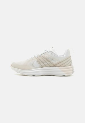 Baskets blanches de sport avec dessus en mesh, logo Nike swoosh sur le côté, semelle rembourrée et languette de traction au talon sur un fond uni.