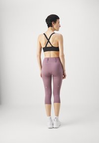 Sujetador deportivo negro con tirantes entrecruzados, combinado con leggings de media pantorrilla en un ligero tono púrpura que cuentan con acentos reflectantes y un ajuste ceñido.