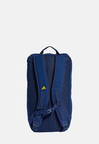 Mörkblå ryggsäck med vadderad mesh-bak och axelremmar, justerbara spännen och en gul logotypaccents. Rektangulär form med förstärkta handtag.