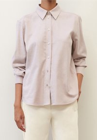 Camicia button-up rosa chiaro con colletto, maniche lunghe e vestibilità comoda. Realizzata in un tessuto morbido con una sottile texture e dettagli con bottoni.