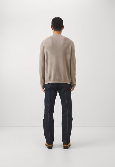 Μπεζ πλεκτό πουλόβερ με υφασμάτινο σχέδιο, συνδυασμένο με σκούρα μπλε τζιν με αντίθετα ραφές. Ορατά καφέ παπούτσια.