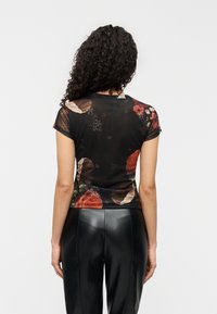 Μαύρο διαφανές τοπ με ανθικά σχέδια σε κόκκινους και πράσινους τόνους, με κοντά μανίκια, εφαρμοστή γραμμή, συνδυασμένο με γυαλιστερό μαύρο κολάν.