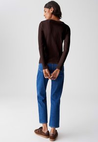 Brown ribbed long-sleeve top paired with blue straight-leg jeans and brown sneakers. The top features a round neckline and fitted silhouette.