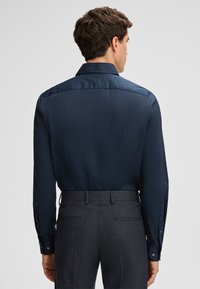 Donkerblauwe, langemouwen shirt met een stevige textuur en een standaardkraag. Het heeft knopenmanchetten en is gecombineerd met grijs gestreepte broek.