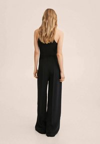 Zwarte, mouwloze jumpsuit met wijde pijpen. Het materiaal lijkt soepel met een aansluitende taille en subtiele naaddetails aan de achterkant.