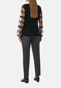 Schwarze Bluse mit sheer gestreiften Ärmeln, kombiniert mit dunkelgrauen Hosen. Die Bluse hat strukturierte horizontale Streifen und einen weichen Schnitt.