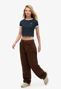 Camiseta de algodón azul marino recortada con ribete blanco, combinada con pantalones sueltos marrón oscuro. El modelo lleva zapatillas de color claro. Diseño sencillo, ajuste casual.