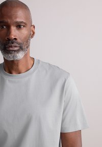 Világosszürke pamut póló kerek nyakkivágással és rövid ujjakkal. Simaságú anyag minimális varrási részletekkel. Egyszerű kialakítás.