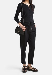 Černý kardigan na knoflíky, černé kalhoty se šňůrkou a černé sandály na pásky. Doplňky tvoří malá černá kabelka a perlový náhrdelník.