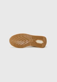 Semelle de chaussure en caoutchouc texturé, avec un motif de semelle en zigzag et une accent de couleur claire près du talon.