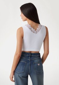 White ribbed crop top featuring a lace V-neck design. Worn with high-waisted blue denim jeans. Focus on texture and contrasting materials.