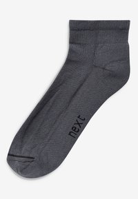 Grå ankelstrømpe lavet af blødt, strækbart materiale. Har en ribbet kant og subtil branding i sort på siden. Glat tekstur generelt.