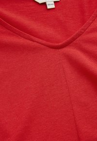 Punainen V-kaula-aukkoinen T-paita, joka on valmistettu pehmeästä ja sileästä kankaasta. Siinä on keskimmäinen sauma, joka kulkee pystysuoraan, ja koon etiketti 38/40.