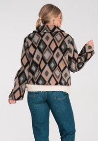 Fleecejacke mit einem abstrakten Rautenmuster in Beige, Schwarz und Blau, ausgestattet mit einem weichen, cremefarbenen unteren Saum und weiten Ärmeln.