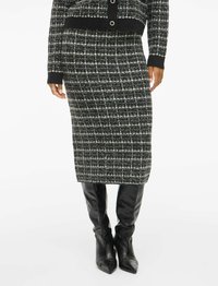 Jupe tricotée à motifs noir et blanc avec une coupe droite, associée à des bottes noires en cuir à talons pointus. Tissu texturé avec un éclat subtil.