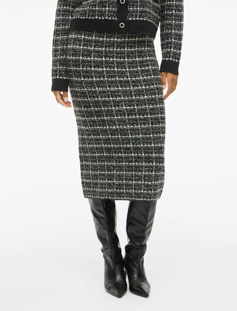 Jupe tricotée à motifs noir et blanc avec une coupe droite, associée à des bottes noires en cuir à talons pointus. Tissu texturé avec un éclat subtil.