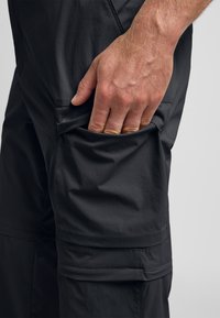 Pantaloni cargo leggeri neri in tessuto testurizzato, con una tasca laterale accessibile da una mano. Linee di design ergonomico su misura.