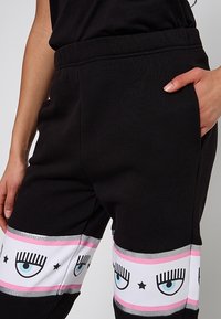 Svarta joggerbyxor i en mjuk bomullsblandning, med ett dekorativt nedre band som visar tecknade ögon och stjärnor i rosa och silverdetaljer.