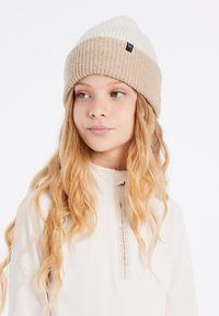 Gebreide muts met een twee-kleurig ontwerp, met een crèmekleurige bovenkant en een taupe geribde band. Gemaakt van zacht materiaal met een klein merkje op de band.