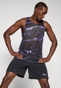 Top negro sin mangas con un patrón abstracto púrpura, hecho de una tela ligera. Combinado con shorts negros que tienen un logotipo blanco de Puma.