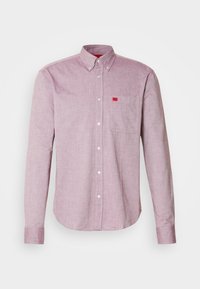 Chemise à manches longues avec boutons, de couleur rose clair, dotée d'un col boutonné et d'une poche poitrine avec une petite étiquette rouge.