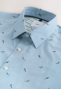 Chemise bleu clair à boutons avec petits imprimés d'oiseaux et col à revers, étiquetée comme coupe régulière taille medium de la marque Next.